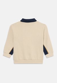 Sudadera beige con cuello marino y paneles laterales en color marino. Cuenta con puños y dobladillo elásticos. Textura suave con detalles de costura.