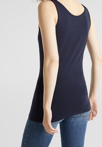 Top senza maniche blu navy con scollatura a girocollo, realizzato in tessuto elasticizzato, caratterizzato da un design aderente e un orlo dritto, abbinato a jeans in denim.