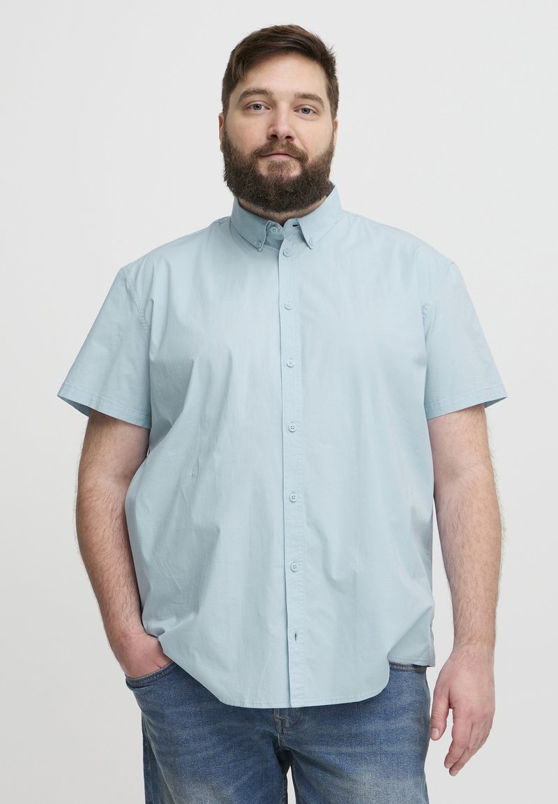 Cămașă cu mânecă scurtă, de culoare albastru deschis, cu guler, cu nasturi pe față, confecționată dintr-un material de bumbac neted, purtată peste blugi. Culoarea principală este albastru deschis.