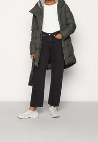 Zelená péřová bunda s kapucí, bílý žebrovaný top, černé džíny s vysokým pasem a šedé tenisky. Černá kabelka. Jednoduchý, funkční design.