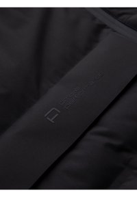 Gros plan sur un tissu noir avec le logo "ombre performance" embossé sur une section de matériau lisse et rembourré.