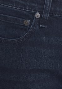 Donkerblauwe denim jeans met een voorzak, metalen knoopsluiting en subtiele textuur. De stof lijkt glad met een lichte glans.