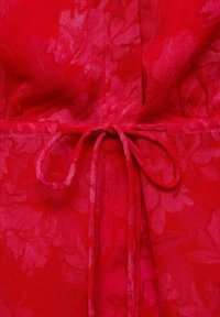 Gros plan d’un tissu rouge à motifs floraux noué en un simple nœud avec des lanières étroites au centre.