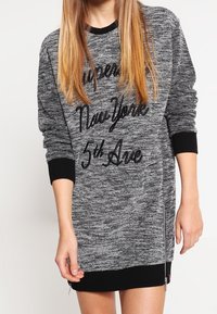 Sweatshirtkleid aus schwarzem und grauem Melange-Stoff, mit Rundhals, langen Ärmeln und schwarzem Aufdruck "Super New York 5th Ave". Schwarze Rippbündchen an den Ärmeln und am Saum.