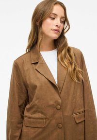 Hnědý, umělý sukně blazer s klopovými límci, dvěma předními kapsami a dvěma knoflíky. Hladká textura, volný střih a minimalistický design.
