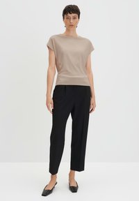 Top beige a maniche corte con scollatura rotonda, abbinato a pantaloni neri a vita alta e scarpe nere a punta.