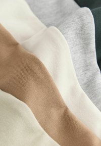Tissus tricotés pliés en beige, crème, gris clair et vert foncé, disposés en couches superposées.