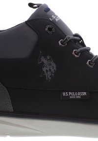 Černé a šedé tenisky U.S. Polo Assn. se šněrováním, kovovými očky a logem jezdce na koni nad značkovou nálepkou na bočním panelu.