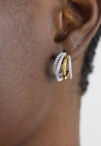 Primo piano di un orecchio che indossa orecchini a cerchio a strati, uno in oro e due incastonati con piccoli diamanti.