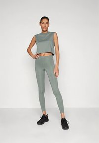 Īss, bez piedurknēm tops un augsta vidukļa legingi maigi zaļā audumā. Gluda un eleganta dizaina, kombinēts ar melnām sporta kurpēm.