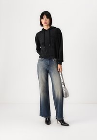Sudadera con capucha negra, vaqueros de pierna ancha azul claro, tacones negros de punta y un bolso de mano plateado. Tejido suave con un corte holgado.
