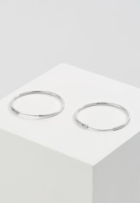 Zilveren creolen met een minimalistisch ontwerp, cirkelvorm, gladde textuur en een veilige sluiting, tentoongesteld op een witte voet.