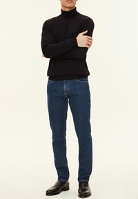 Schwarzer Rollkragenpullover mit enganliegender Passform, kombiniert mit dunkelblauen Jeans und schwarzen Lederschuhen, was einen klassischen, lässigen Look ergibt.
