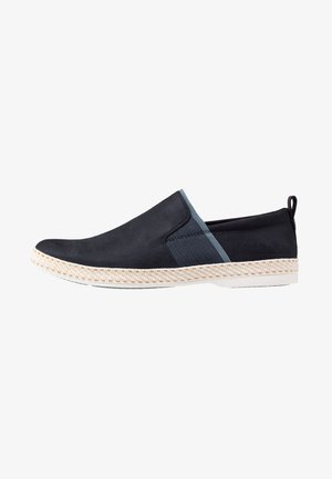 Black slip-on shoe with elastic side panels, a woven jute midsole, and a textured upper. Features a rear pull tab for easy wear.