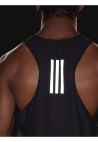 Débardeur sportif noir avec une texture en mesh respirant, comportant trois bandes réfléchissantes blanches dans le dos. Conçu avec des emmanchures dégagées.