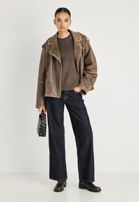 Καφέ δερμάτινο μπουφάν biker με ασημένιες μεταλλικές λεπτομέρειες, συνδυασμένο με καφέ πουλόβερ και σκούρο τζιν φαρδιάς γραμμής. Μαύρη τσάντα με καρφιά.