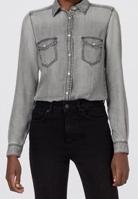 Gray denim button-up shirt with long sleeves, two chest pockets, and contrasting stitch details; paired with black jeans.