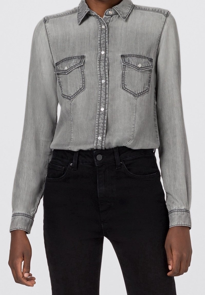 Gray denim button-up shirt with long sleeves, two chest pockets, and contrasting stitch details; paired with black jeans.