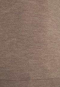 Nahaufnahme von weichem, braunem Strickstoff mit feiner Naht und geripptem Saumdetail.