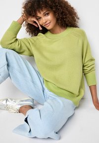 Limonengrüner gestrickter Pullover mit gerippten Bündchen und Saum, kombiniert mit hellblauen übergroßen Jeans und metallisch silbernen Turnschuhen.