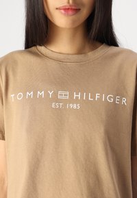 Ruda medvilninė marškinėliai su balta užrašu "TOMMY HILFIGER EST. 1985" ir logotipu. Apvalus iškirpimas, trumpi rankovės, lygus paviršius.