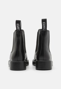 Juodi odiniai auliniai batai su elastingomis šoninėmis dalimis, traukimo kilpelėmis ir tekstūruotu guminio pado dizainu. Minimalistinis dizainas su elegantiška silueto forma.