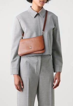 Borsa a tracolla in pelle marrone con una texture liscia, forma rettangolare, emblema d'ape argentata e tracolla regolabile, indossata sopra una camicia a quadri.