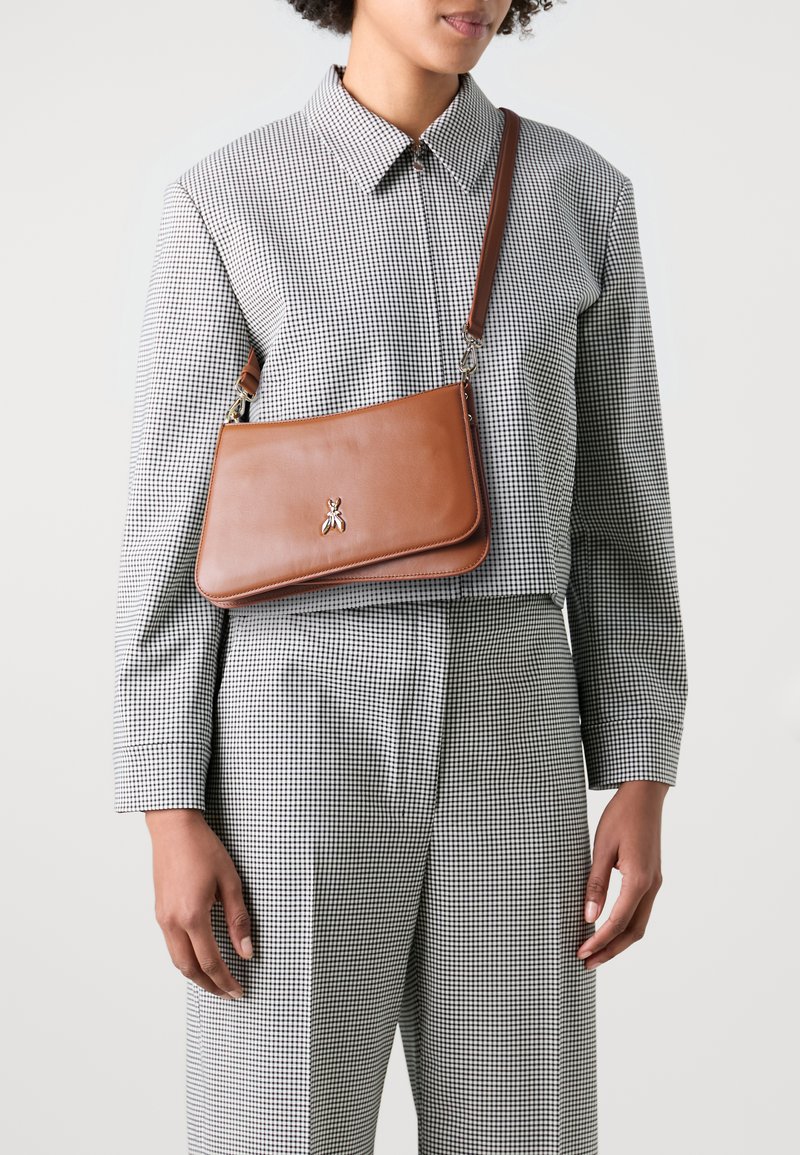 Borsa a tracolla in pelle marrone con una texture liscia, forma rettangolare, emblema d'ape argentata e tracolla regolabile, indossata sopra una camicia a quadri.