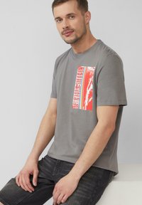 Grijze katoenen T-shirt met ronde hals, voorzien van een rechthoekige rode grafische print met tekst op de voorkant. Korte mouwen, relaxed fit.