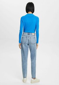 Maglietta blu a maniche lunghe con una texture a coste abbinata a jeans azzurri a vita alta con due tasche posteriori e una vestibilità rilassata.