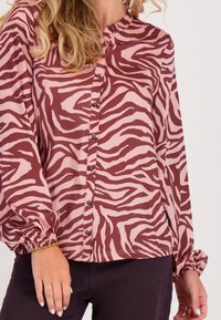 Langarm blouse in bordeauxrood en lichtroze zebra print, met een ronde halslijn en knoopsluitingen aan de voorkant. Soepele stof en gathered manchetten.