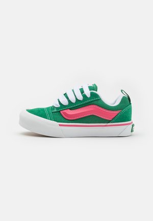 Zapatillas de lona verdes con cordones blancos, acentos rosas y una suela de goma blanca. Presentan un logo bordado en el lateral y una parte superior texturizada.