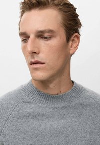 Maglione lavorato a maglia grigio chiaro con collo rotondo e polsini a coste. Textura morbida e finitura liscia, con maniche a raglan.