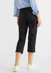 Černé zkrácené kalhoty s hladkým, texturovaným povrchem, s zadními kapsami a bočními švy, doplněné o bílé tenisky.