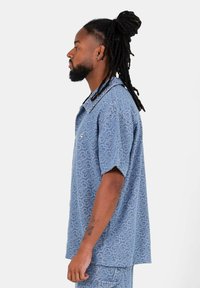 Blauwe kortemouwenshirt met patroon, gemaakt van een gestructureerde stof met een kraag, met een subtiel hartontwerp en een knoopdetail op de borst.