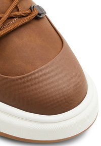 Zapatilla texturizada marrón con una puntera suave, suela de goma blanca y cordones y herrajes en marrón oscuro en contraste.