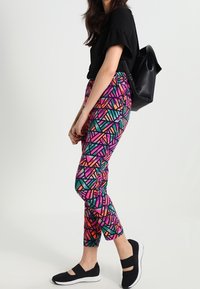 Barevné kalhoty s geometrickým vzorem v růžové, zelené a oranžové barvě, vyrobené z elastického materiálu. V kombinaci s černým topem a teniskami.