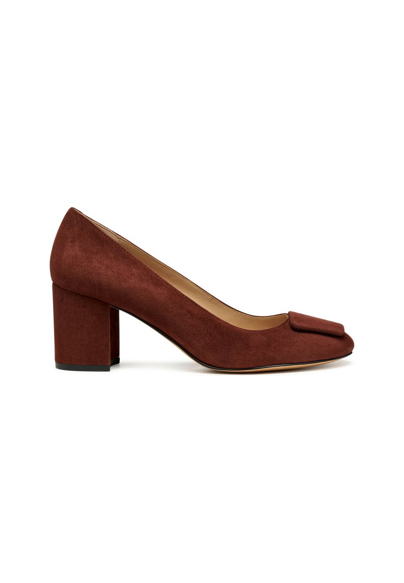 Zapato de ante marrón con tacón bloque y punta redondeada, adornado con un lazo en la parte superior. Textura suave con un ligero brillo y una estructura robusta.
