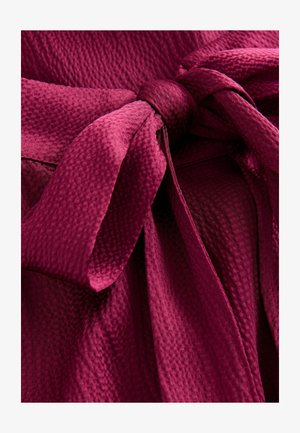 Burgundy textured fabric with a tied bow detail; features a soft, wrinkled appearance and a smooth surface with a subtle sheen.
