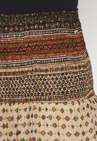 Patterned skirt featuring a smocked waistband in earthy tones with intricate designs. Lightweight fabric adorned with small floral patterns.