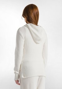 Felpa bianca a maglia con cappuccio, polsini e orlo a coste. Texture morbida e vestibilità rilassata, dettagli di cucitura visibili lungo i lati.