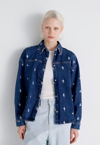 Casaco de ganga com bordados florais em azul claro e branco, apresentando um decote com colarinho, fecho de botão e mangas longas.