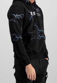 Czarna bluza z kapturem z niebieskim nadrukiem pioruna, kieszenią typu kangur i sznurkiem przy kapturze. Materiał z mieszanki bawełny, ściągacze na rękawach i u dołu.