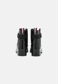 Bottines noires brillantes à semelles épaisses, avec des côtés élastiques, des détails de sangle et des tirettes rouges, blanches et bleues à l'arrière.