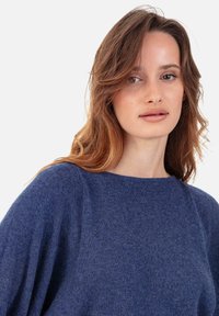 Blauer, gestrickter Pullover mit rundem Ausschnitt und lockerer Passform. Weiche Textur, überschnittene Schultern und dezente Rippenstrickdetails entlang der Nähte.