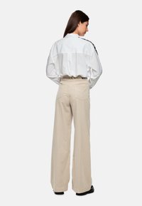 White oversized shirt with wide cuffs, beige wide-leg pants, and black shoes. The shirt has a back yoke and a subtle texture.