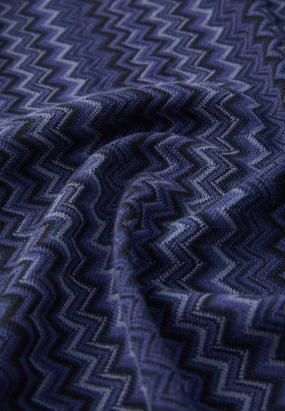 Tessuto con motivo a zigzag blu, caratterizzato da una texture morbida con diverse sfumature di blu e nero. La tessitura crea un'apparenza tridimensionale.