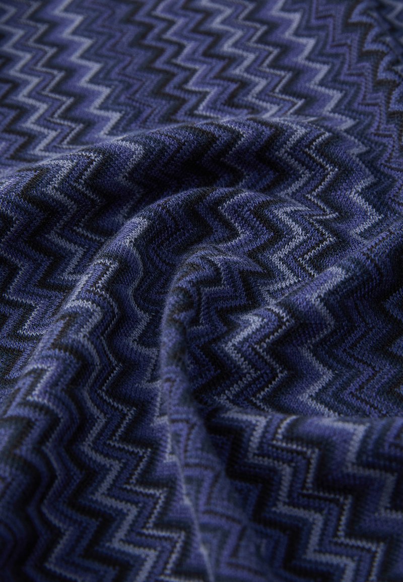 Blaues Stoff mit Zickzack-Muster, das eine weiche Textur mit verschiedenen Blautönen und Schwarz aufweist. Das Gewebe erzeugt eine dreidimensionale Optik.