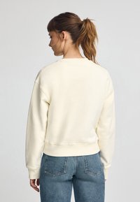 Suéter crema de corte relajado, con puños y dobladillo acanalados, textura suave y cuello redondo, combinado con jeans de talle alto en azul claro.