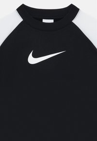 Maglietta sportiva nera con maniche raglan bianche, dotata di un grande logo Nike bianco sul petto. Texture liscia e colletto a giro.